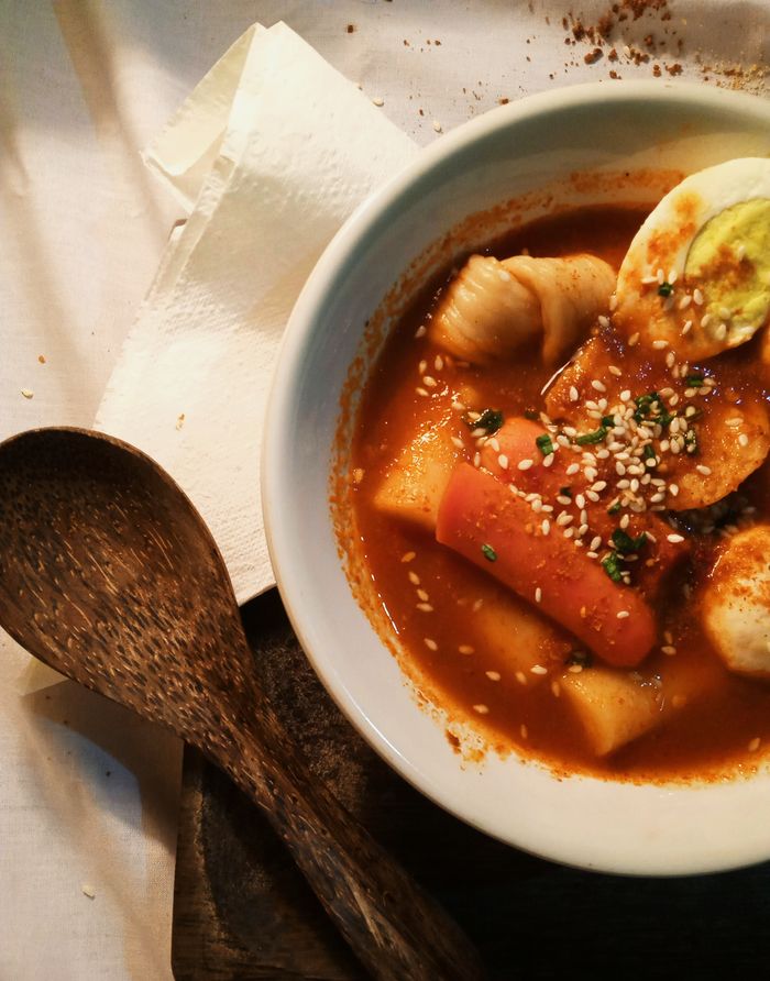 services-04 A mouthwatering bowl of spicy Korean Tteokbokki garnished with sesame seeds and herbs.