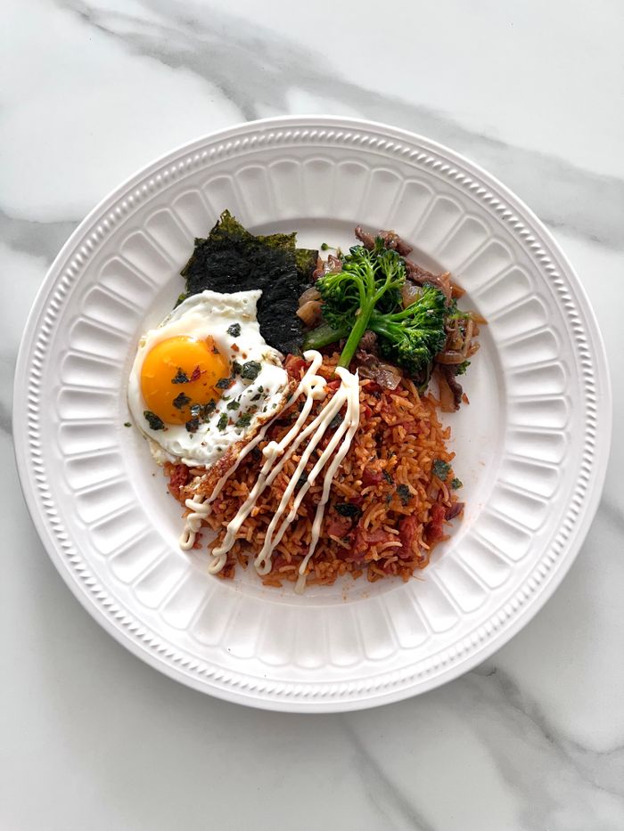 Delicious Korean kimchi fried rice with fried egg and seaweed on a white plate.